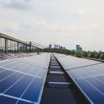 Photograph of solar panels on a roof with a city skyline in the background.