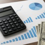 Calculator next to graphs and dollar bills on a wooden surface